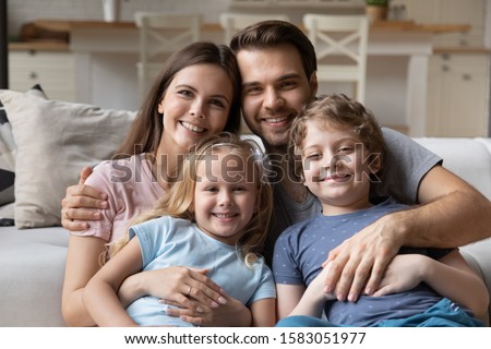 Beautiful married couple and little pre-school children pretty son and sweet daughter sitting on couch looking at camera feels happy. Concept of welfare full family portrait, new home, capture moment