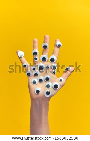 Plastic eyes glued on a woman's hand on an yellow background, copy space. Sign language concept.