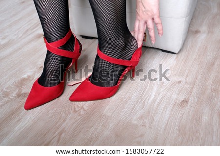 Woman in black fishnet stockings trying on red shoes on high heels. Concept of shoe size, female fashion, tired legs or foot pain
