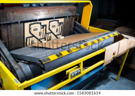 A punching machine in a cardboard boxes factory production hall. Paper die cutting machine. Royalty-Free Stock Photo #1583081614