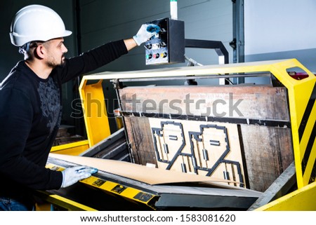 Worker in a hard hat turning on a punching machine. Cardboard boxes factory. Paper die cutting machine Royalty-Free Stock Photo #1583081620