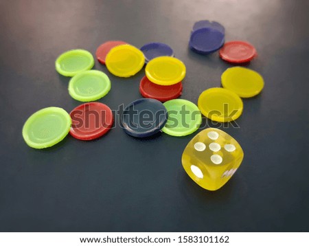 Yellow ludo dice and colorful tokens isolated on blue background