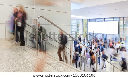 Many anonymous people are walking on a staircase in front of a web poster at a trade fair