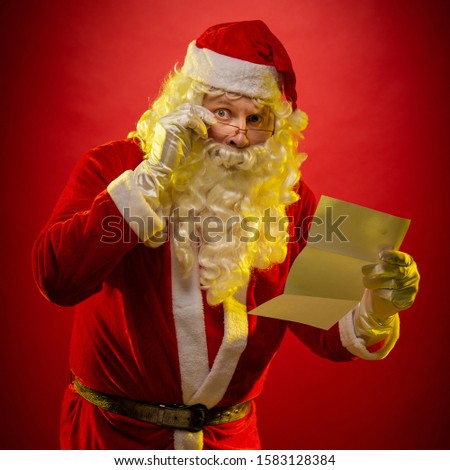 Santa Claus holds a sheet of paper in his hands a Christmas letter reads and poses on a dark red background