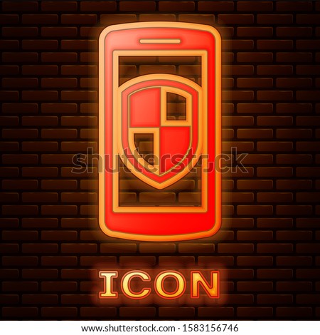 Glowing neon Smartphone, mobile phone with security shield icon isolated on brick wall background.  