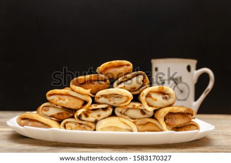 Homemade pancakes with filling stacked in a pyramid on a white plate against a black wall with a Cup, copy space