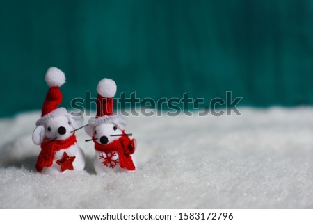  Two white mice in red Christmas caps and scarfs on the snow. Green background.