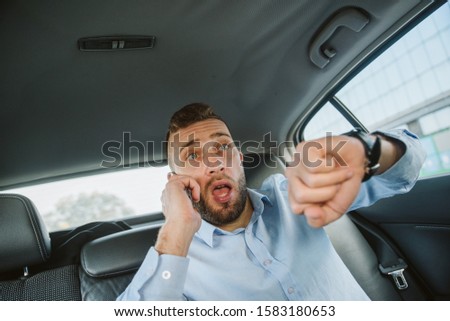 A portrait of a young businessman in a blue shirt sitting in the back seat of a car and late for work