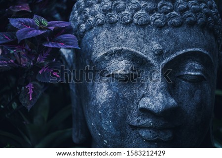 Stone Buddha face close-up in trend blue color toning. Handmade carved Buddha statue in balinese garden as decoration.