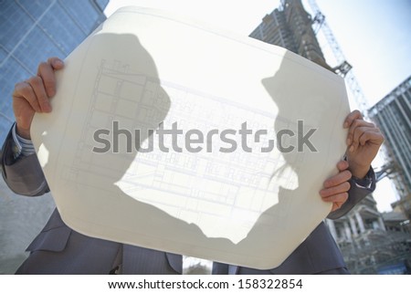 Two architects at construction site holding blueprint