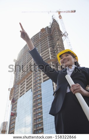 Young female architect pointing at construction site
