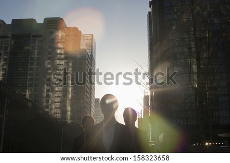 Three business people walking down city street with sunlight at their back