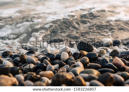 Small stones by the sea with bokeh effect. Blurred decorative background, place for text. Summer wallpaper, sunny sunset light