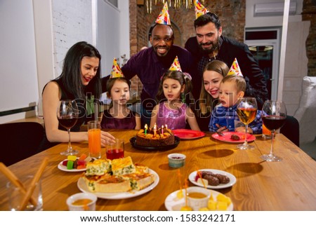 Portrait of happy multiethnic family celebrating a birthday at home. Big family eating snacks and drinking wine while greeting and having fun children. Celebration, family, party, home concept.
