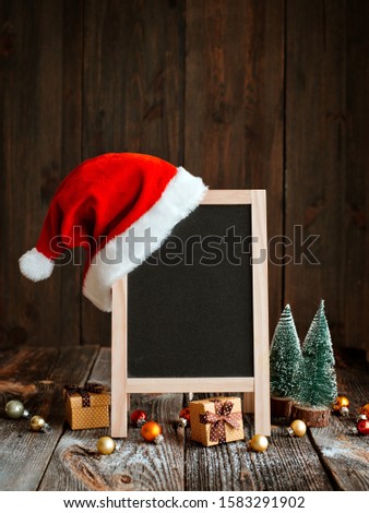 Christmas mockup layout for happy new year. Festive composition with xmas decorations and snow with empty space for text. Black chalkboard frame with red Santa hat