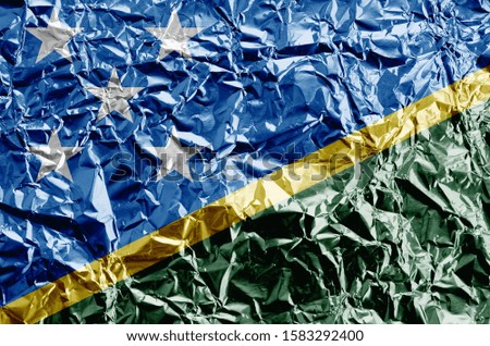 Solomon Islands flag depicted in paint colors on shiny crumpled aluminium foil closeup. Textured banner on rough background