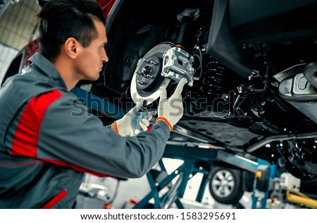 Car mechanic worker repairing suspension of lifted automobile at auto repair garage shop station Royalty-Free Stock Photo #1583295691