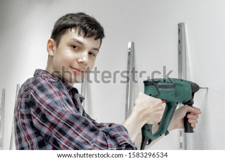 A teenager works as a builder, holding a drill or perforator. Concept of child labour, choice of profession