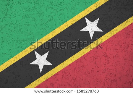 Saint Kitts and Nevis flag depicted in bright paint colors on old relief plastering wall. Textured banner on rough background