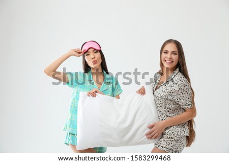 Beautiful women in pajamas with pillow on light grey background. Bedtime