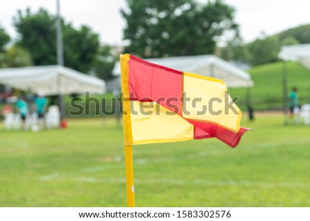 Soccer field corner flag in foreground. Background blurred with unrecognisable football players. Sports and people theme.