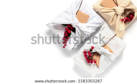 Christmas gifts wrapped in light textile and decorated Christmas branches with berries, flat lay, copy space. Christmas gifts in eco-friendly packaging on a white background, top view,