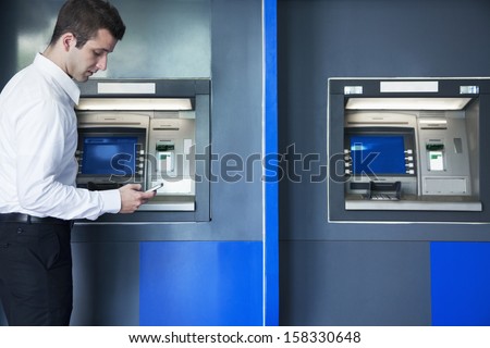 Young businessman taking out money from ATM 