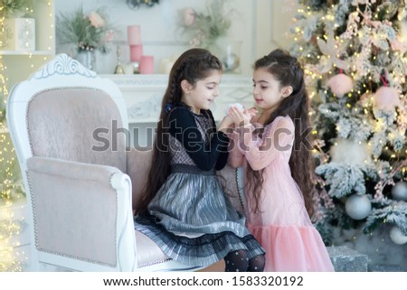 Two baby girl in festive attire is in the room decorated for the new year and Christmas. The concept of holidays and gifts.