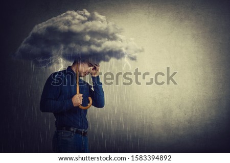 Pessimistic man, standing under rain, suffering anxiety as holding an umbrella thunderstorm cloud over head. Concept of memory loss and dementia disease. Alzheimer's losing brain and memory function. Royalty-Free Stock Photo #1583394892