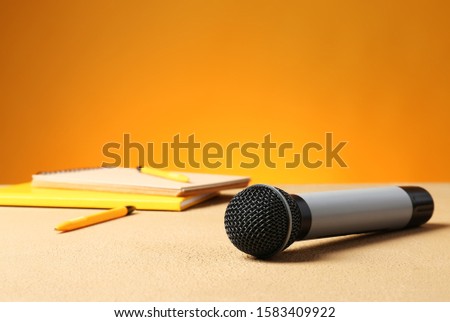 Microphone and notebooks on table against color background