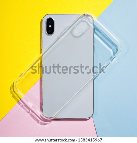 Clear iPhone case mock up. Smart phone on a background of pink, yellow and blue paper, silicone transparent case back view mockup Royalty-Free Stock Photo #1583415967