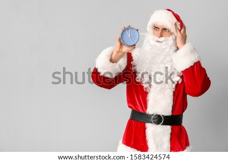 Confused Santa Claus with alarm clock on light background. Christmas countdown concept