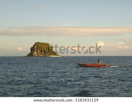 A wide shot of a person riding a canoe on the body of water near a small islet under a blue sky with clouds