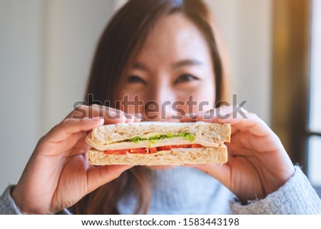 A beautiful woman holding a piece of whole wheat sandwich cover her face
