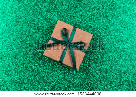 Craft gift box with green bow on sparkle green background. Holiday concept. Flat lay. Place for text.