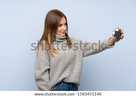 Teenager girl with sweater over isolated blue background making a selfie