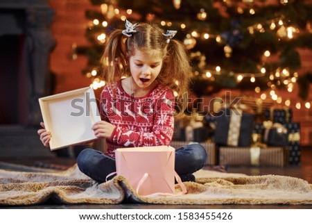 Cute little girl sits in the decorated christmas room opening gift box.