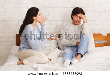 Mood Swings During Pregnancy Concept. Angry pregnant woman arguing with her tired husband, blaming him for everything while sitting on bed together Royalty-Free Stock Photo #1583458093