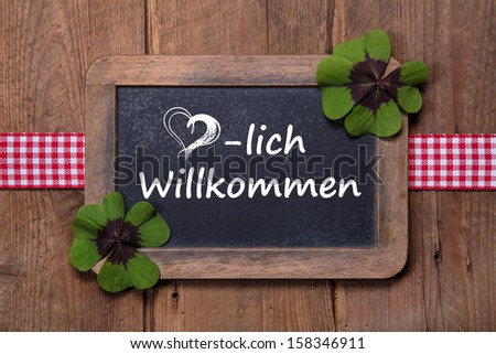 Old menu board with welcome message in german - clovers and ribbon on wooden background