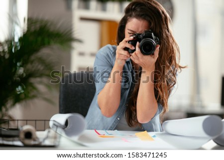 Happy young female executive looking at camera in creative office.
Freelance photographer woman with camera at home office editing photos on computer