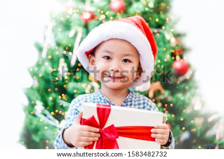 Little asian toddler boy smile and excited and holding red gift box on christmas tree and white background.Boy child holding gift box in Christmas celebration and Happy New year concept.