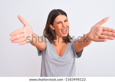 Portrait of beautiful young woman standing over isolated white background looking at the camera smiling with open arms for hug. Cheerful expression embracing happiness.