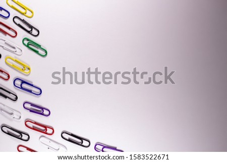 Colored paper clips for product advertising. Metal office clips attach, on a light background. Stationery fix tool for page, card. The equipment for documentation.