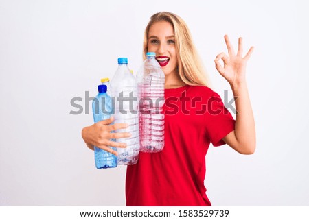 Young beautiful woman recycling plastic bottles standing over isolated white background doing ok sign with fingers, excellent symbol
