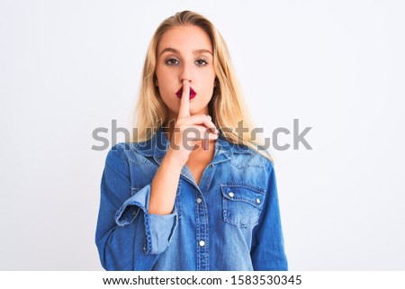 Young beautiful woman wearing casual denim shirt standing over isolated white background asking to be quiet with finger on lips. Silence and secret concept.