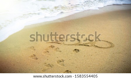 Happy New Year 2020, lettering on the beach with sea wave. Numbers 2020 year on the sea shore, message handwritten in the golden sand on beautiful beach background. New Years concept. Sandy footprint.