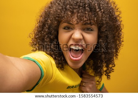 Brazil supporter. Brazilian woman fan celebrating on soccer, football match on yellow background. Brazil colors. Selfie smartphone.