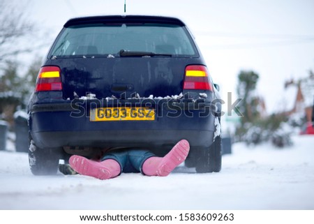 Woman laying underneath car in snow