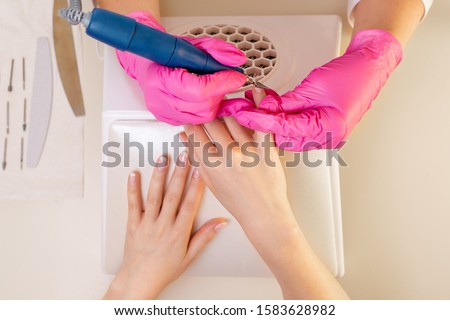 Medicine, cosmetology and manicure. Woman manicure master, in pink gloves doing manicure client in the salon. Cutting the top layer. Hands close up. The view from the to
