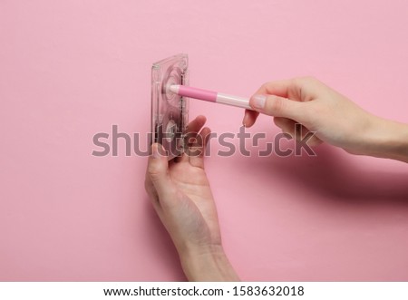 Female hands rewind an audio cassette tape on a pink pastel background. Analog technology of the past